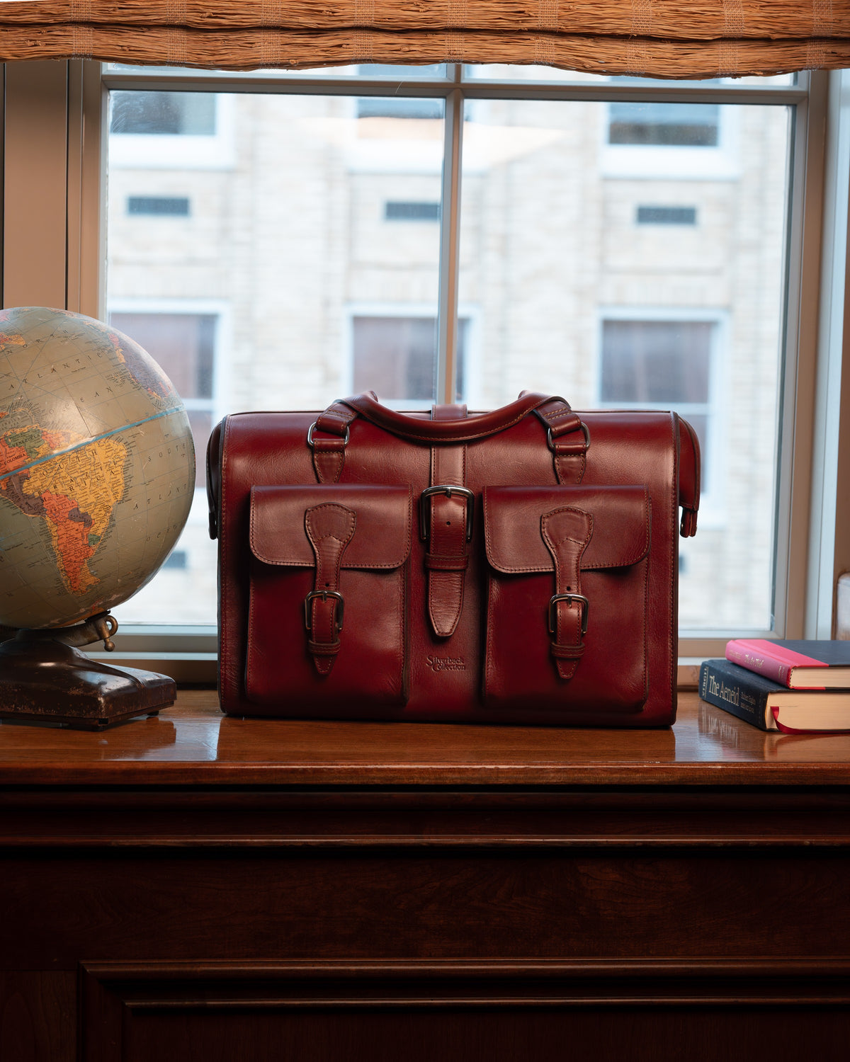 Blackstone Barrister Briefcase in Oxblood, front view on a window desk beside a globe and books