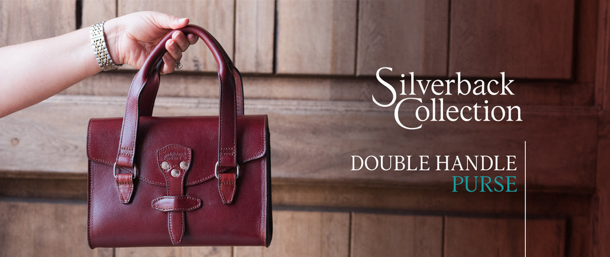 Double Handle Purse-Silverback in Oxblood held up by a hand, banner text Silverback Collection Double Handle Purse