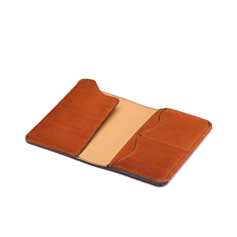 Tan leather passport sleeve lying open at an angle, showing a cream-coloured interior and three card pockets.