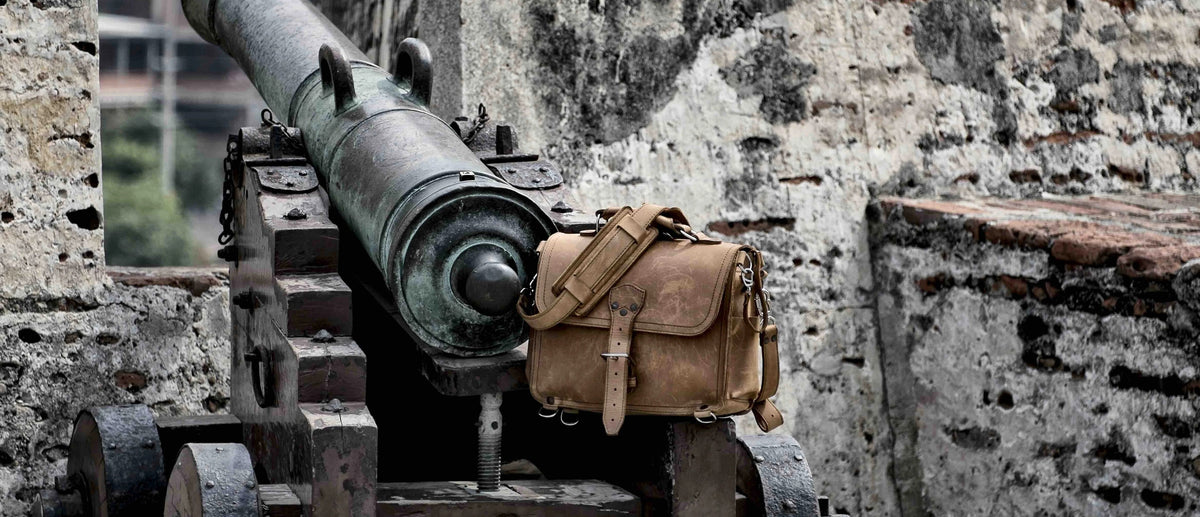 Tan leather slim briefcase resting on an old iron cannon beside a weathered stone wall