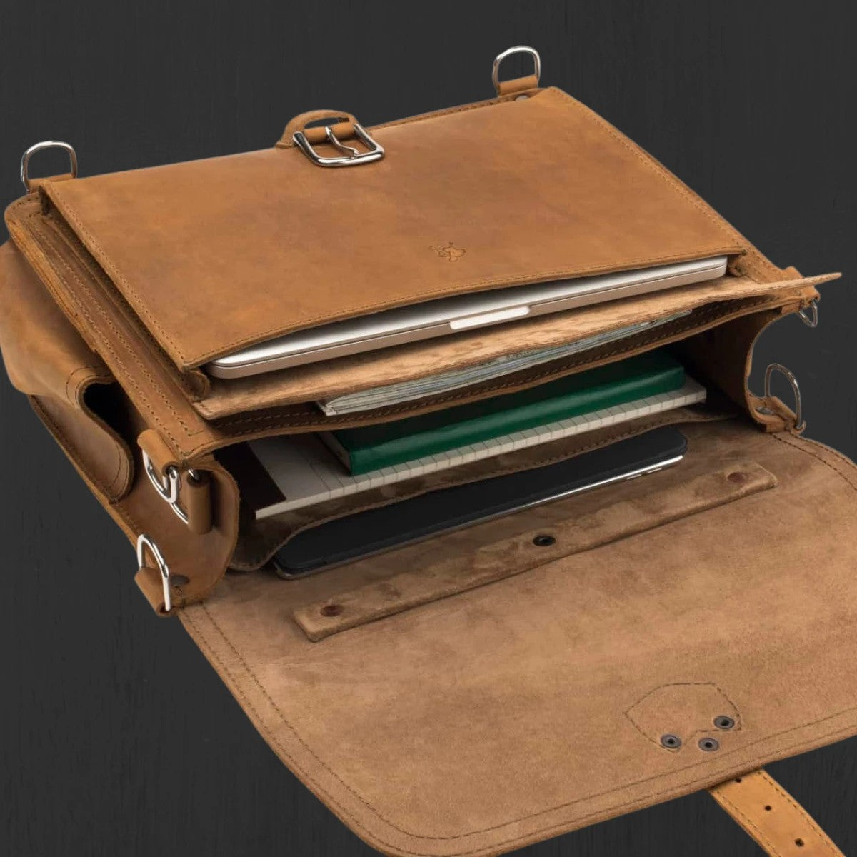 Tan leather slim briefcase with the flap open, holding a laptop, notebooks and documents