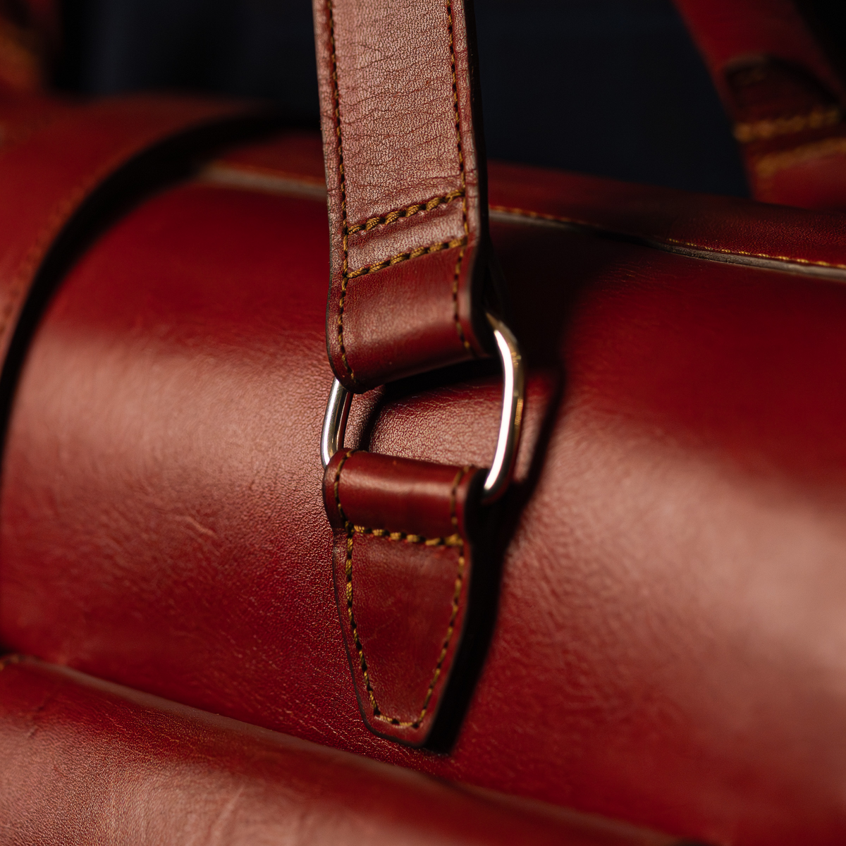 Close-up of a stitched leather strap and silver D-ring hardware on an oxblood leather bag