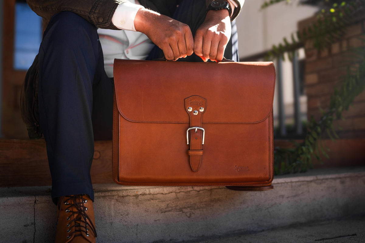 Man seated on outdoor steps holding a natural brown Silverback Livingstone leather briefcase on his lap