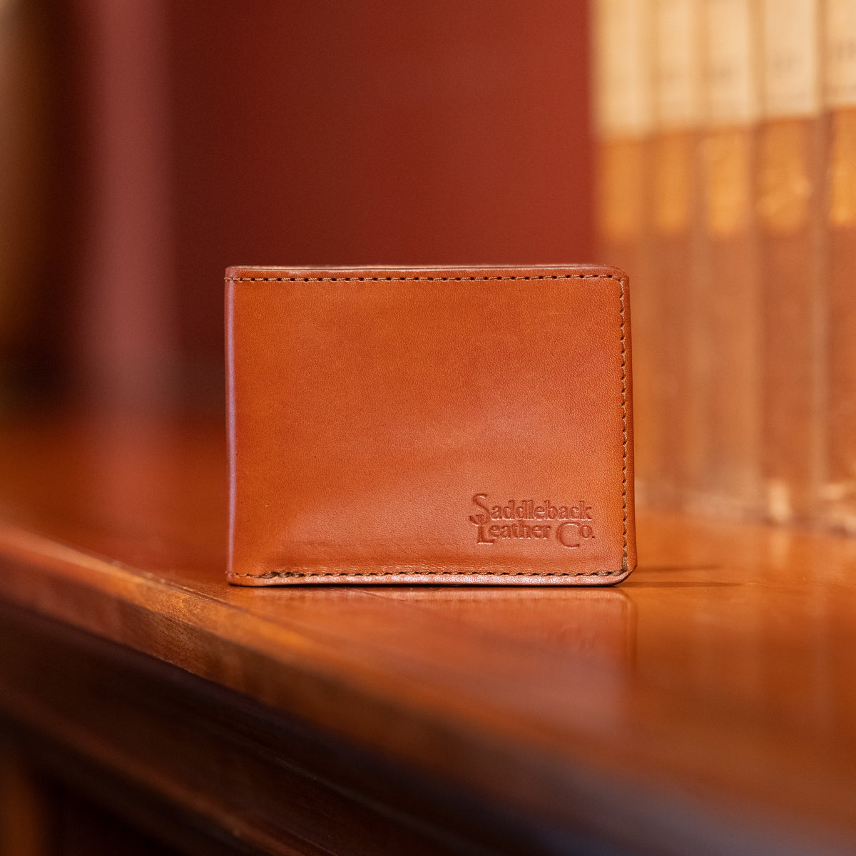 Silverback Penn bifold wallet in natural leather, embossed with the Saddleback Leather Co. logo, standing on a polished wood shelf