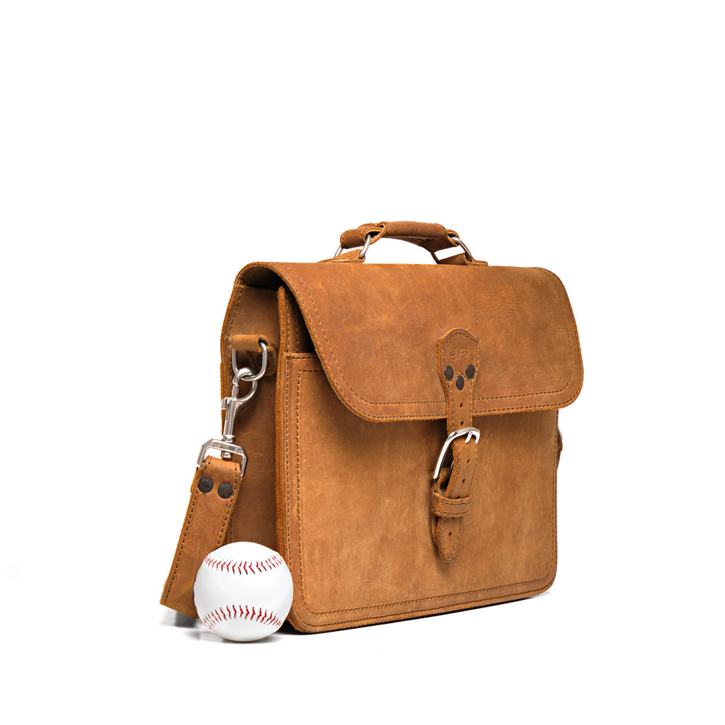 Fourteener Thin Leather Briefcase in Tobacco, angled front view with buckled flap, shown beside a baseball for size
