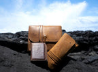 Cash & Receipt Bag in Tobacco on black lava rocks beside other leather goods under a blue sky