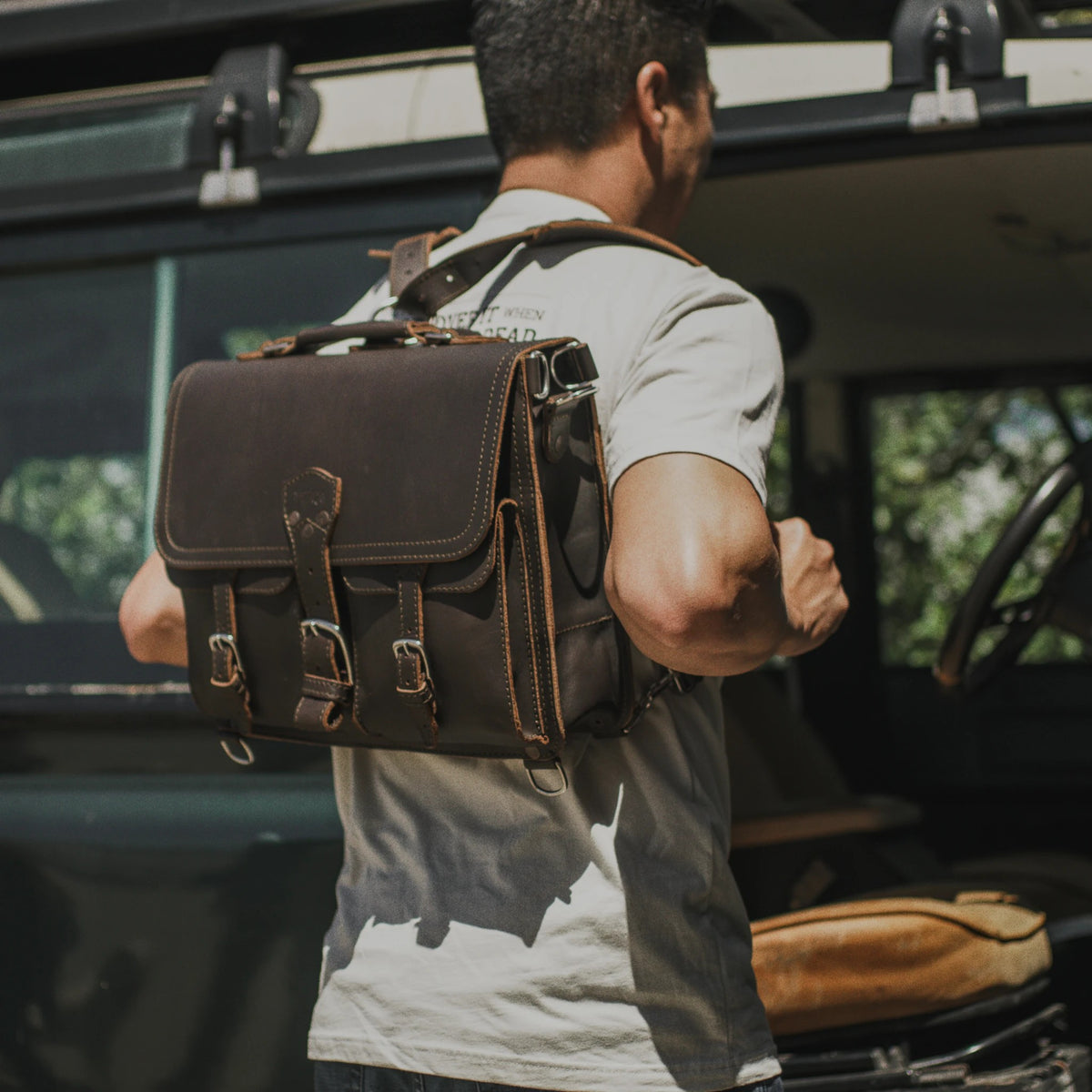 Thin Front Pocket Leather Briefcase in Dark Coffee Brown worn in backpack mode by a man beside an off-road truck