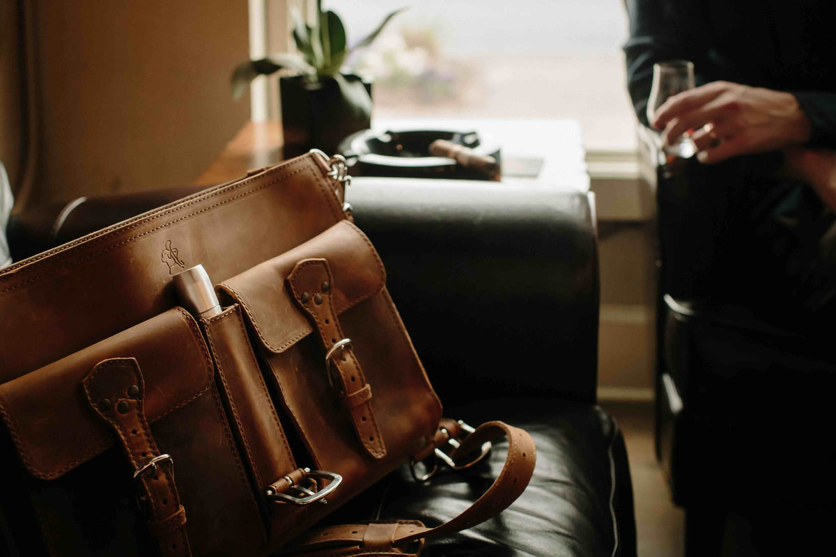 Thin Front Pocket Leather Briefcase in Tobacco on a leather chair with a cigar tucked in a front pocket, dim lounge