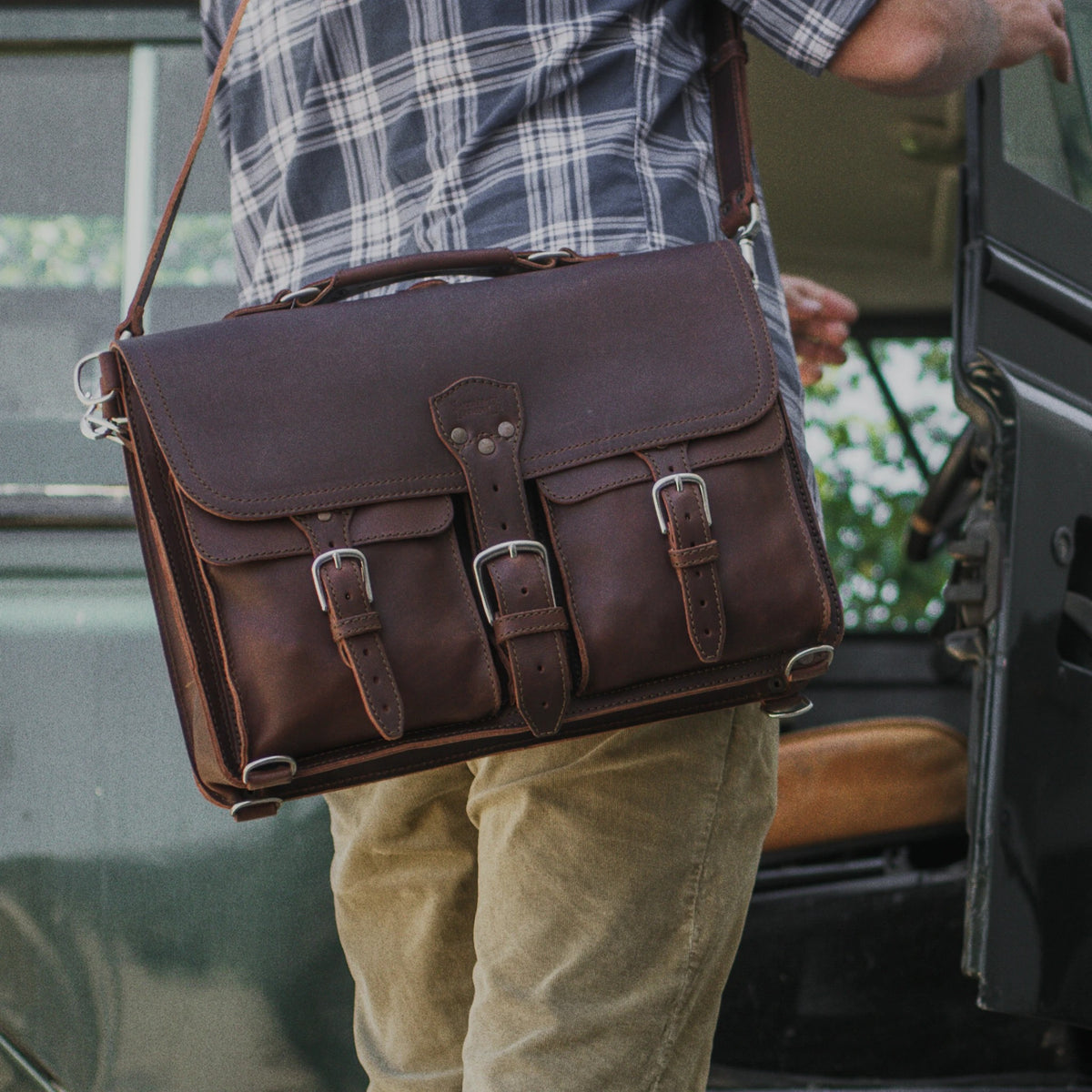 Thin Front Pocket Leather Briefcase in Dark Coffee Brown worn on the shoulder by a person in a plaid shirt by a truck