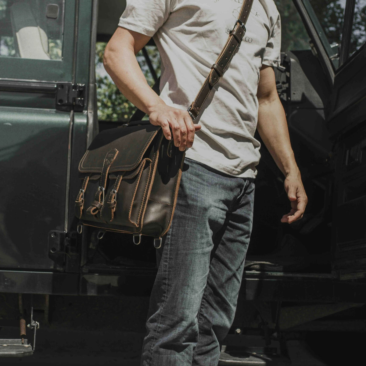 Thin Front Pocket Leather Briefcase in Dark Coffee Brown carried messenger style by a man in a tee beside a truck