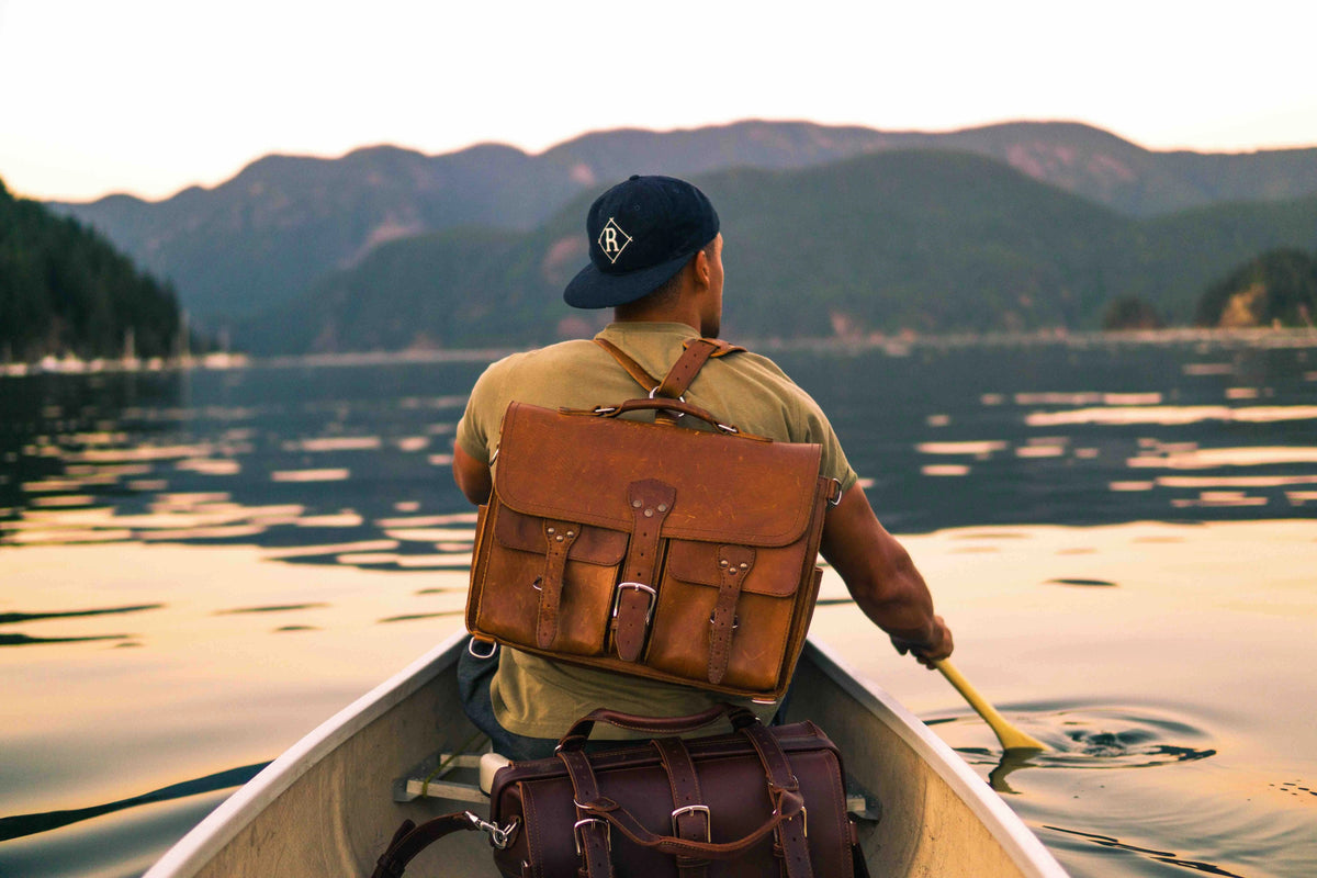 Thin Front Pocket Leather Briefcase in Tobacco worn as a backpack by a man paddling a canoe on a mountain lake