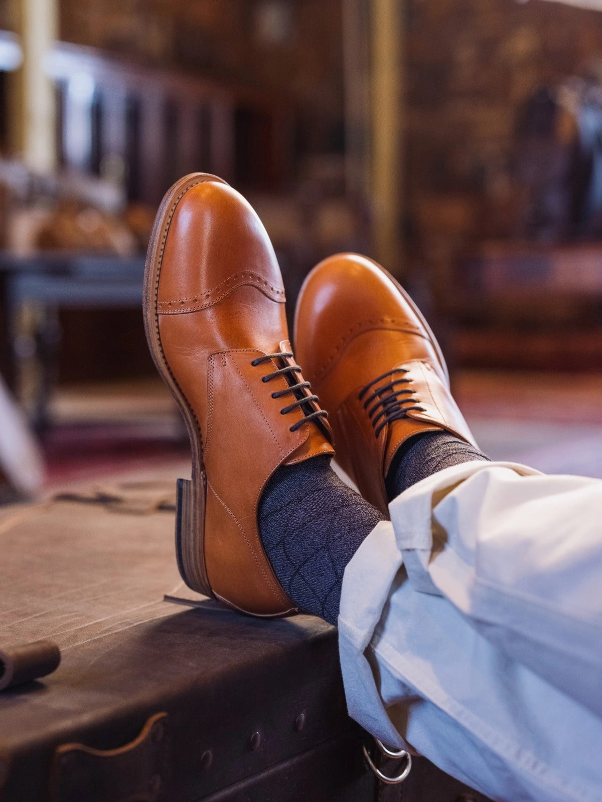 Toe Cap Shoes - English Tan worn with crossed feet resting up on an old leather trunk