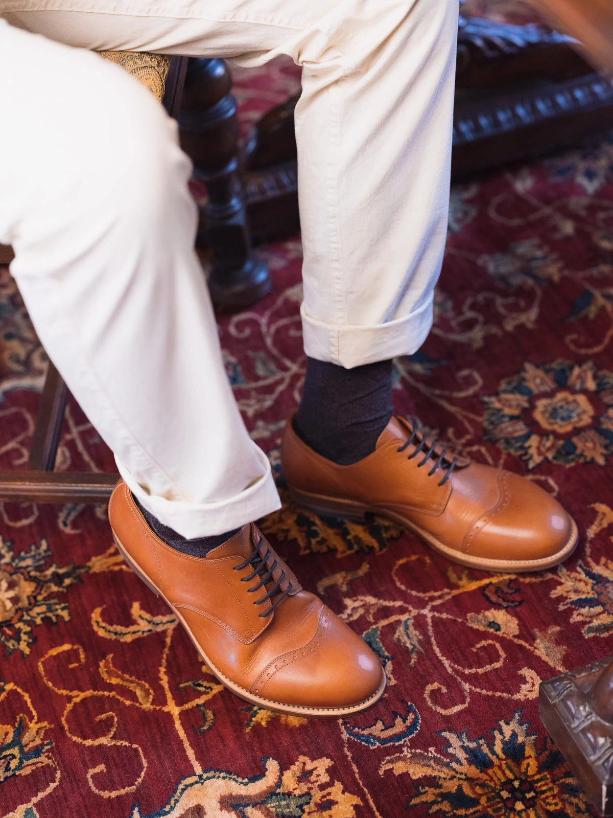 Toe Cap Shoes - English Tan, overhead view on a seated person in cream trousers over a red patterned rug
