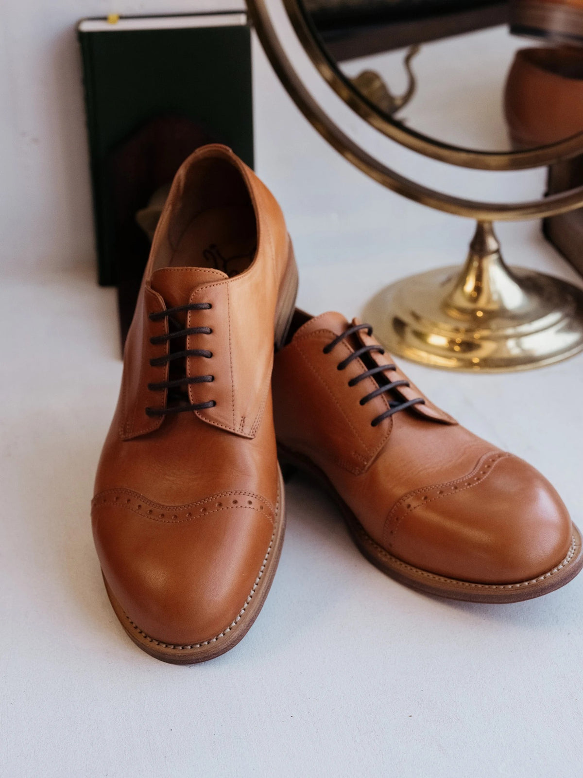 Toe Cap Shoes - English Tan, front view of a laced pair with brogued toe caps beside a brass vanity mirror
