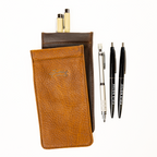 Bear Trap Leather Pen Cases in Tobacco and Dark Coffee Brown, layered beside two pens and a mechanical pencil