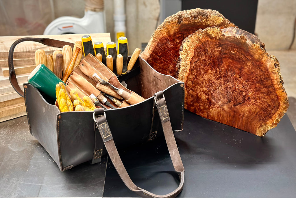 Range and Tool Tote in Dark Coffee Brown on a workbench, filled with carving chisels beside burl wood slabs