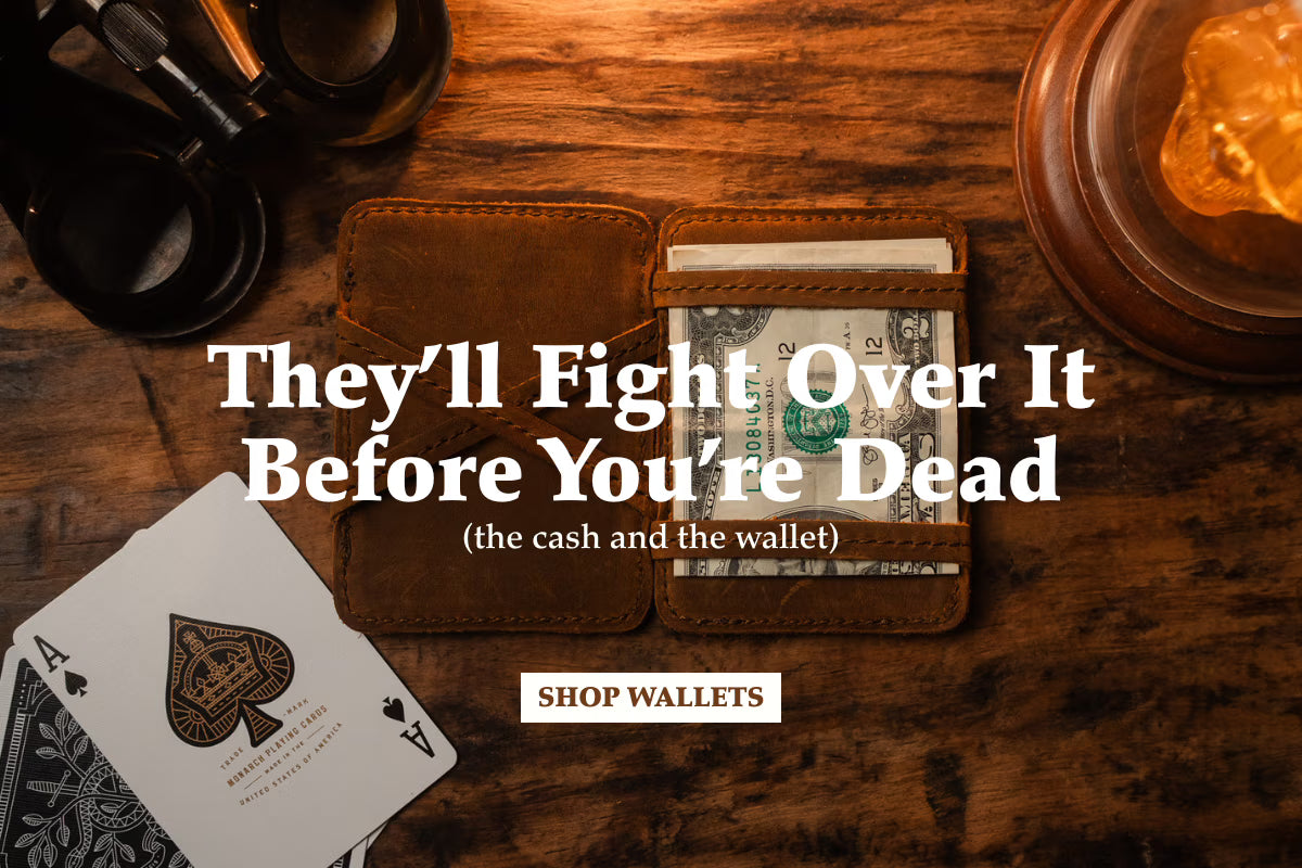 They'll fight over it before you're dead (the cash and the wallet). Shop wallets. A worn leather wallet holding folded dollar bills on a dark wooden table beside playing cards.
