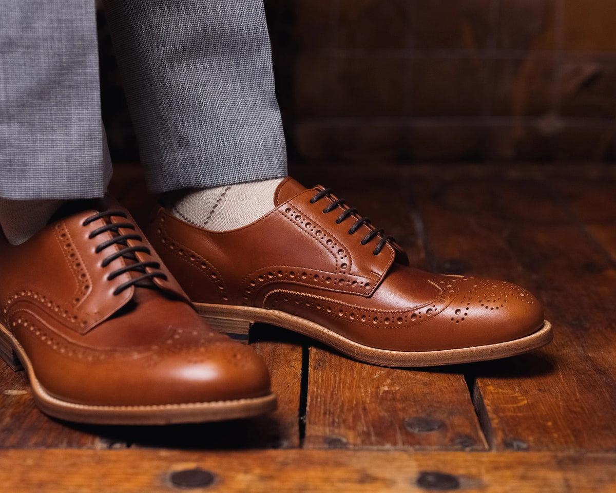 Wingtip Shoes - Natural Tan on foot, close side view of a pair on worn wood planks with grey trousers